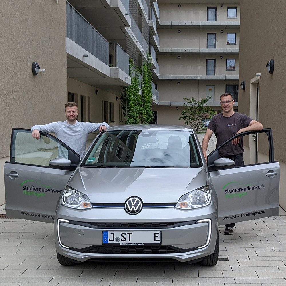 Hannes Nader, Hauswart beim Studierendenwerk Thüringen, nimmt das E-Auto von Matthias Prause, verantwortlich für den Fuhrpark, entgegen 