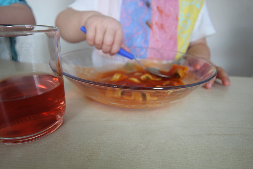 Kinderhände löffeln Essen von einem Teller